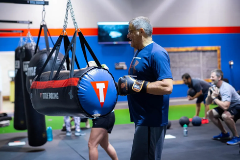 Man boxing heavy bag while others train in group fitness class at Freedom Fitness gym in St. Peters, Missouri