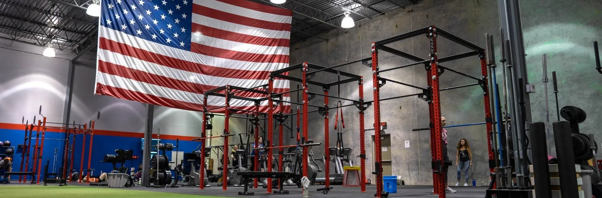 WhatsApp Image 2024-10-03 at 8.57.09 AM Wide view of Freedom Fitness gym floor with squat racks, equipment, and large American flag in St. Peters, Missouri