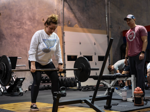 Woman performing barbell deadlift with trainer coaching at Freedom Fitness gym in St. Peters, Missouri