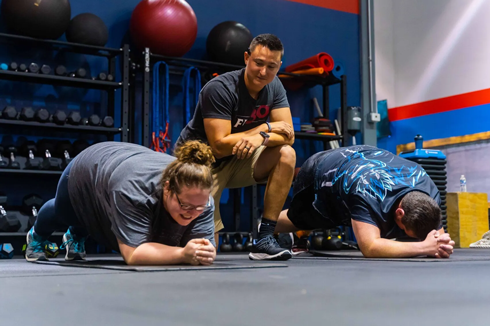 Trainer coaching two people holding plank position during group workout at Freedom Fitness gym in St. Peters, Missouri