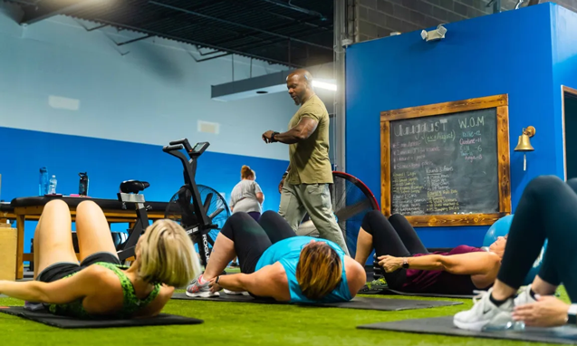 Group fitness class doing floor core exercises with trainer leading at Freedom Fitness gym in St. Peters, Missouri