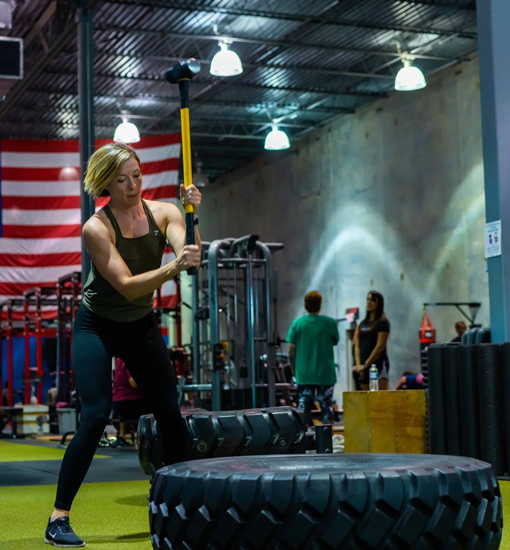 Woman flipping tire with sledgehammer during strength workout at Freedom Fitness gym in St. Peters, Missouri
