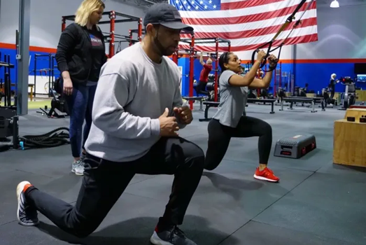 Man and woman performing lunge and suspension training exercises with coach at Freedom Fitness gym in St. Peters, Missouri