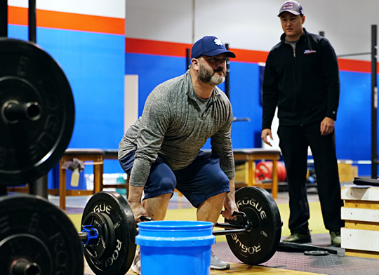 Man performing barbell deadlift with trainer coaching at Freedom Fitness gym in St. Peters, Missouri