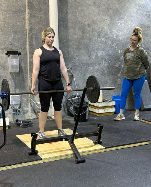 Woman performing barbell deadlift with trainer observing at Freedom Fitness gym in St. Peters, Missouri