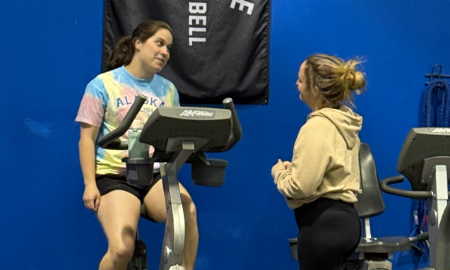 Two women talking during a workout on a stationary bike at Freedom Fitness gym in St. Peters, Missouri